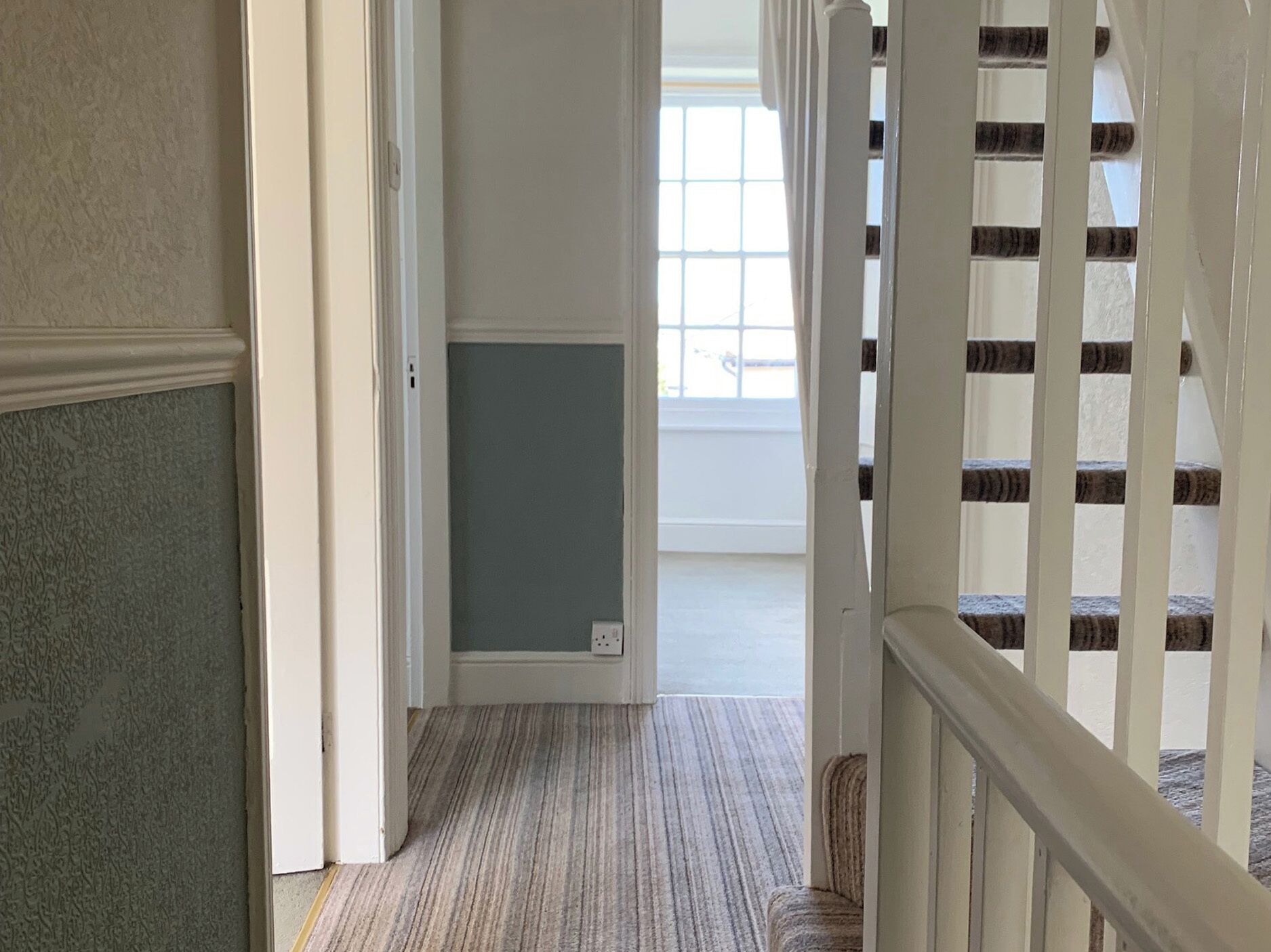 A hallway with a carpeted floor, a white door, and a staircase with white railings.