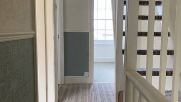 A hallway with a carpeted floor, a white door, and a staircase with white railings.