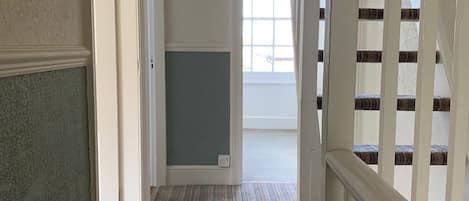 Un pasillo con piso alfombrado, una puerta blanca y una escalera con barandillas blancas.