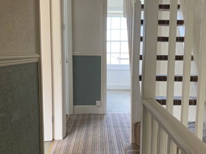 A hallway with a carpeted floor, a white door, and a staircase with white railings. - 3 Newboro Terrace (Conwy)
