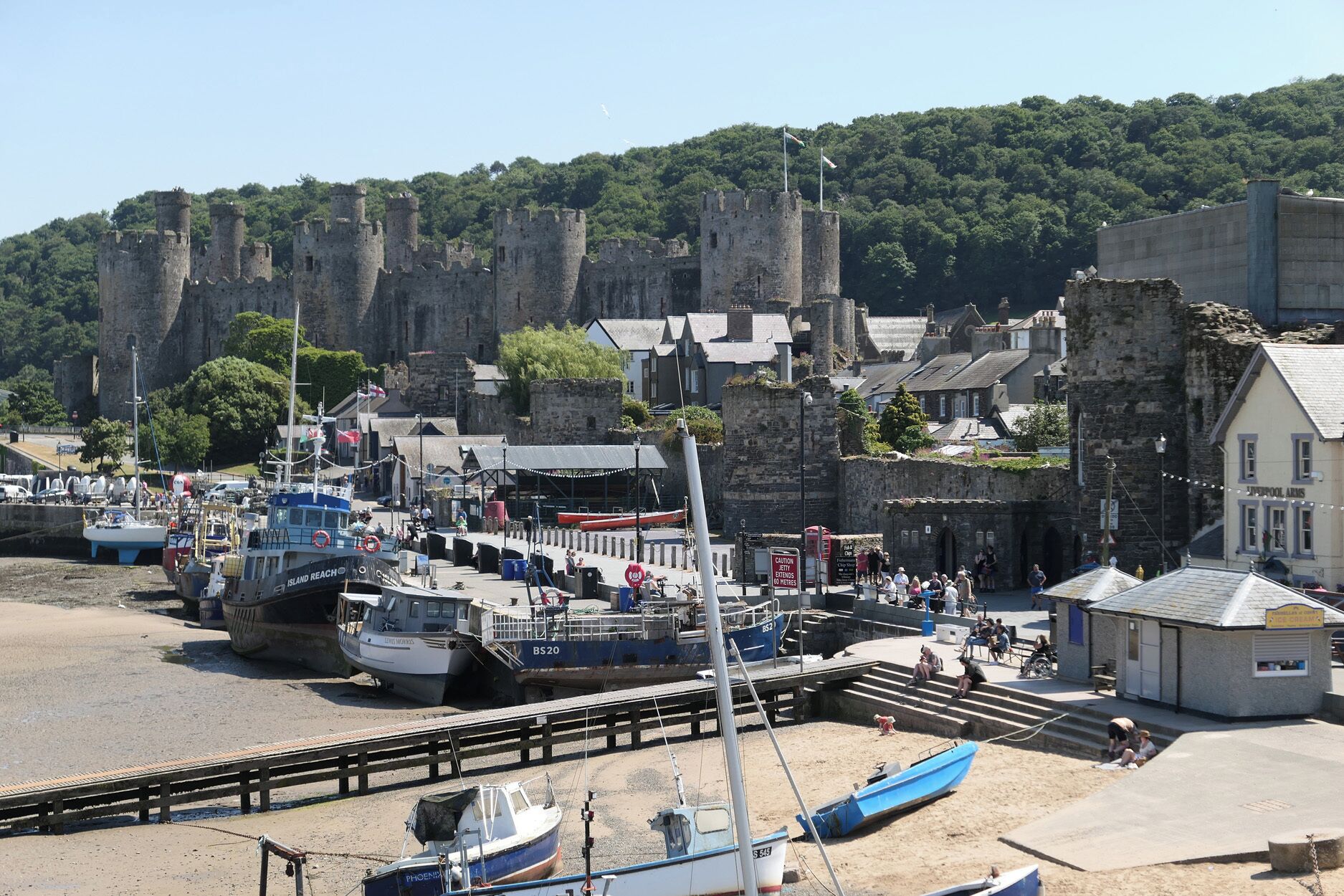 A coastal town with a historic castle, boats docked at the harbor, and a small building labeled 'LIVERPOOL ARMS'.