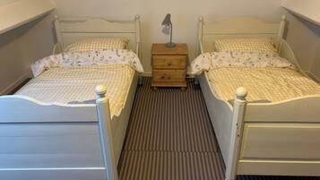 Twin beds with checkered bedding, a nightstand with a lamp, and a striped carpet.