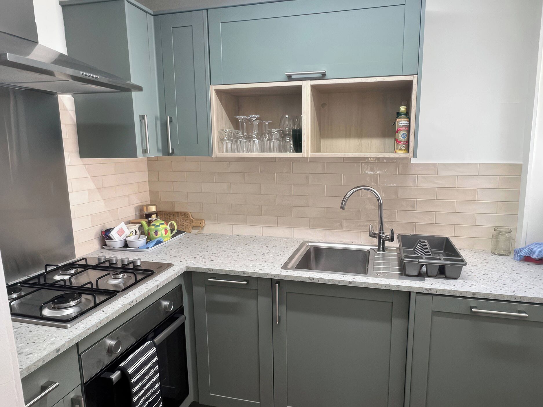 Een keuken met grijze kastjes, een roestvrijstalen afzuigkap, een spoelbak en een aanrecht met een theeservies.