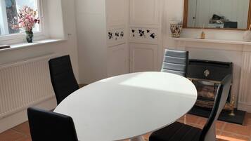A dining area with a round white table, black chairs, a vase with flowers, a radiator, and a mirror on the wall.