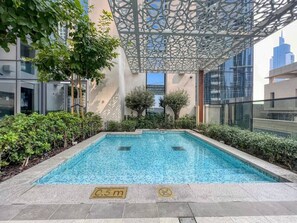 A rectangular pool with a depth marker, surrounded by greenery and modern architecture. - FIRST CLASS | 2BR | near Burj Khalifa & Dubai Mall (Downtown)