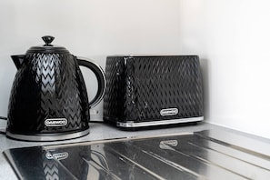 Une bouilloire et un grille-pain électriques de la marque DAEWOO, de couleur noire, posés sur une surface réfléchissante.