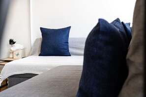 Ein Bett mit einer weiß-grauen Bettdecke, einem blauen Kopfkissen und einer dunkelblauen Decke.