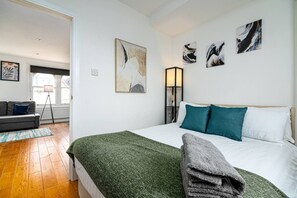 Quarto com cama, duas almofadas, manta verde e obras de arte na parede.