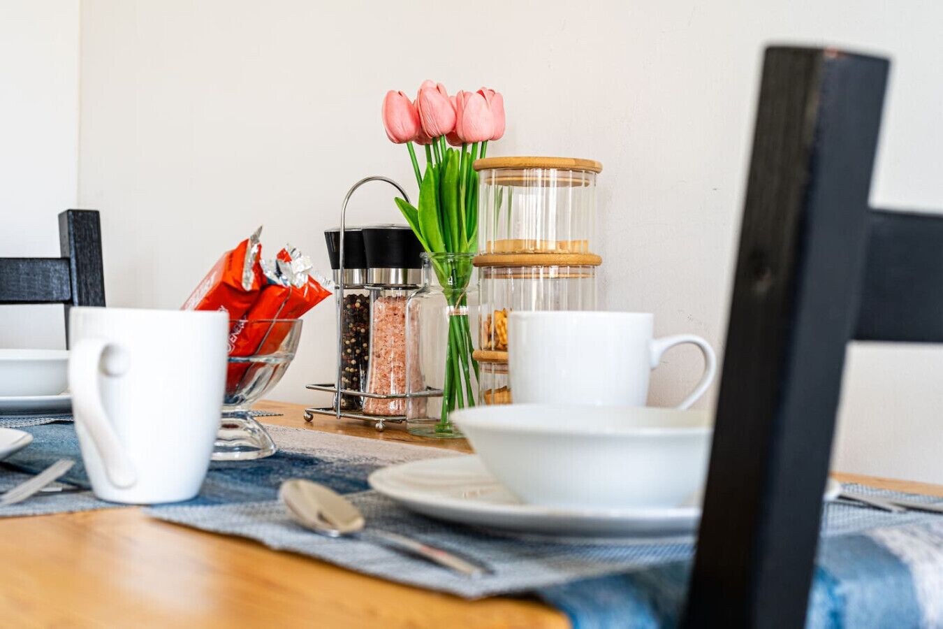 Et spisebord med hvide kopper, et glas med pink tulipaner og en metalkrydderihylde.