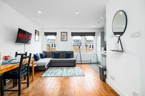 Ein modernes Wohnzimmer mit einer Couch, einem Esstisch mit Stühlen, einem Fernseher und Blick ins Freie.