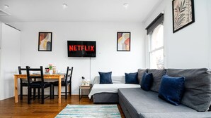 A modern living room with a gray sofa, a wooden dining table, and a flat-screen TV mounted on the wall. - West Hampstead Hub - 1 bedroom spacious apartment (Greater London)