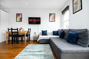 A modern living room with a gray sofa, a wooden dining table, and a flat-screen TV mounted on the wall. - West Hampstead Hub - 1 bedroom spacious apartment (Greater London)