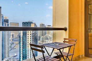 A balcony with a table and chairs, a view of a cityscape, and a building with 'EMAAR' signage. - FIRST CLASS |2BR| Scenic View w/ JBR Beach Access (JBR)