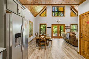 Eine moderne Küche mit Kühlschrank, einem Holzespeisetisch und Stühlen. Es gibt Fenster mit Jalousien, eine Tür mit einer US-amerikanischen Flagge und eine Holzbalkendecke.