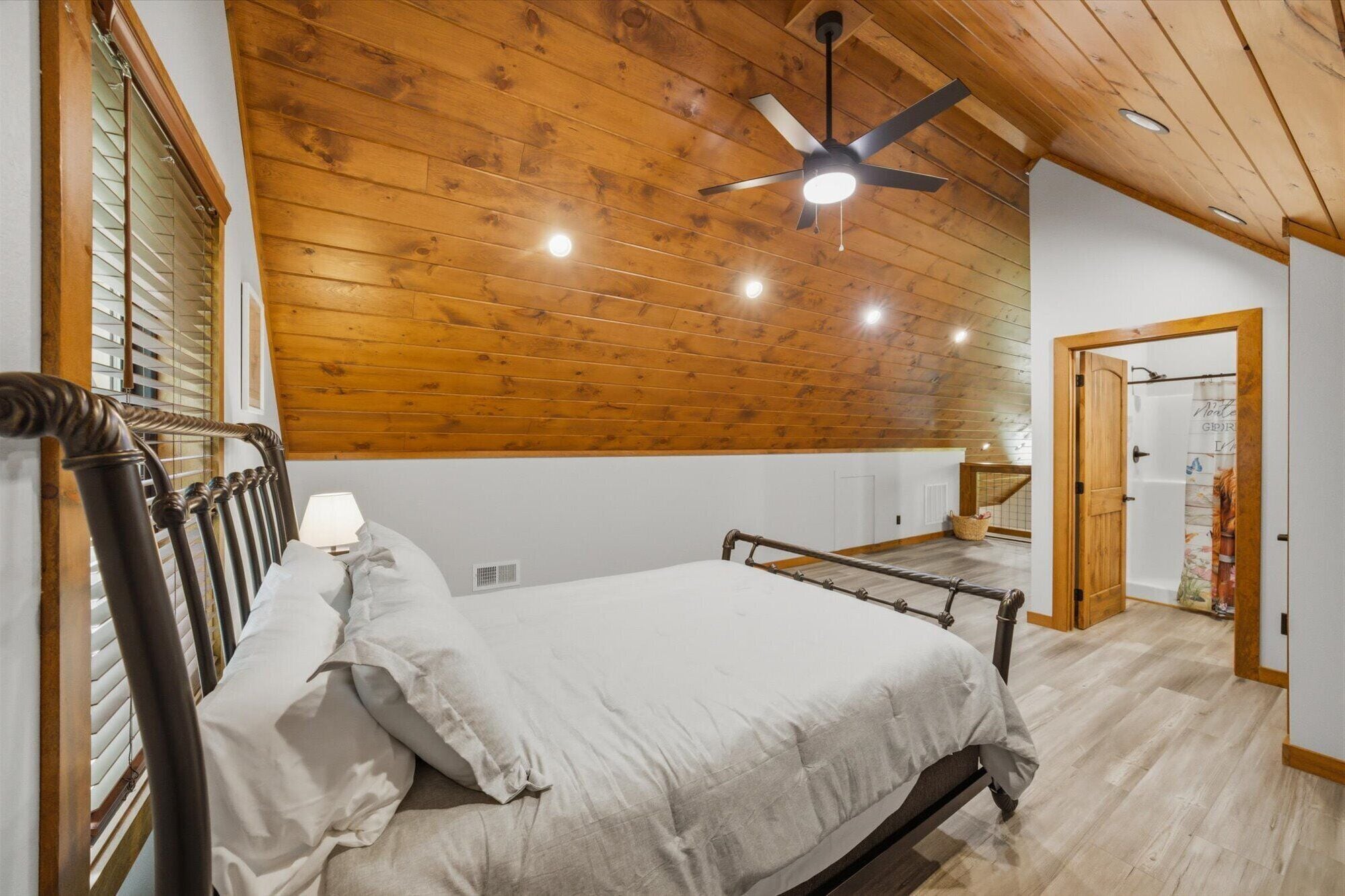 Une chambre avec un plafond en bois, un lit avec une tête de lit, un ventilateur de plafond et une porte ornée d’une affiche.