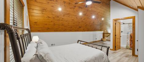 Une chambre avec un plafond en bois, un lit avec une tête de lit, un ventilateur de plafond et une porte ornée d’une affiche.