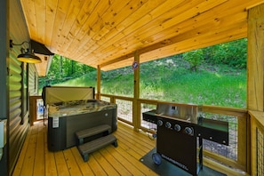 Eine Holterrasse mit Whirlpool, Grill und Blick auf einen Wald.