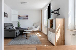 Ein modernes Wohnzimmer mit einer Couch, einem kleinen Tisch, einem Sessel, einem Schrank und einem an der Wand befestigten Fernseher.