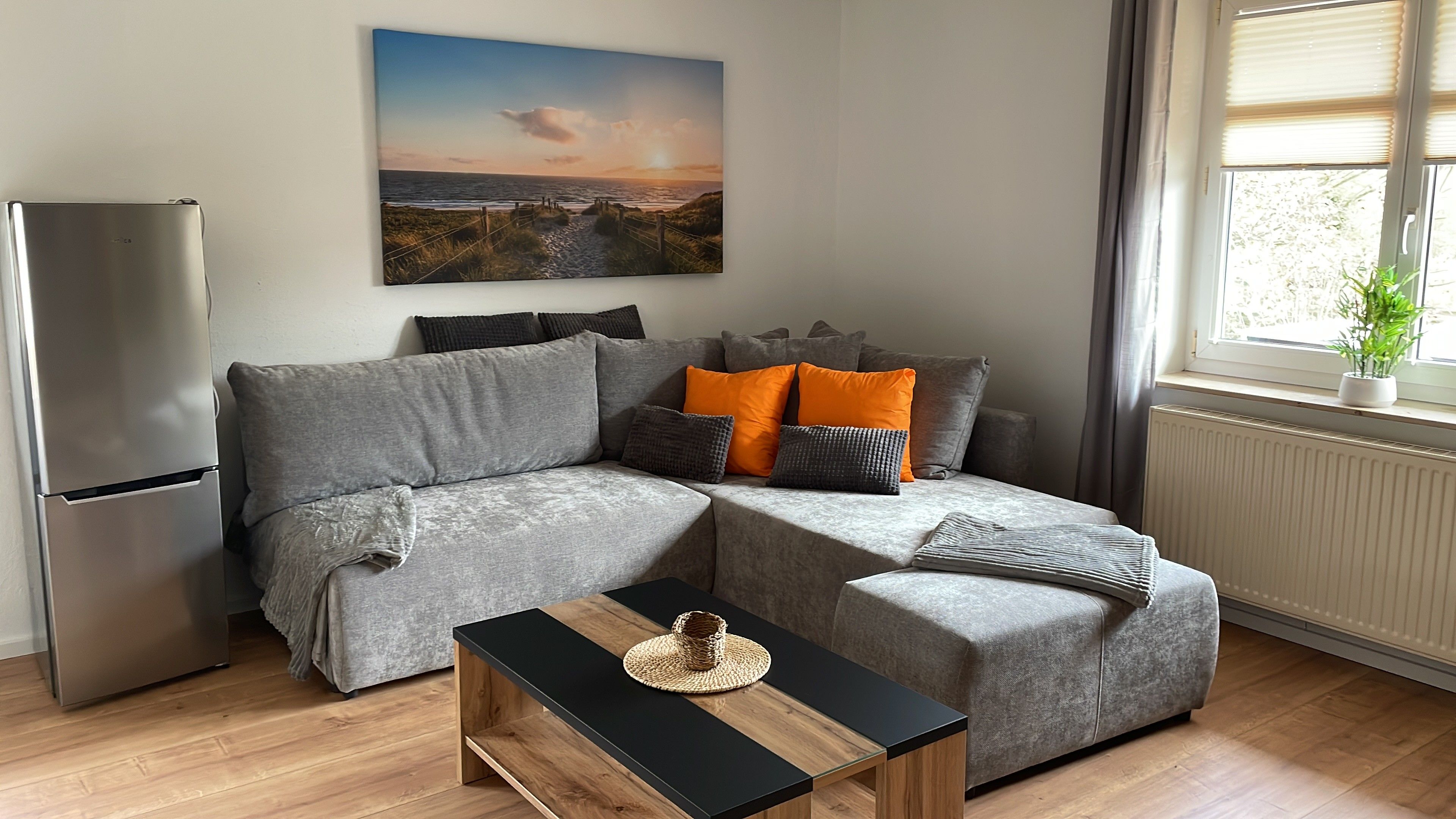 Een moderne woonkamer met een grijze modulaire bank, een klein houten bijzettafeltje en een schilderij van een strandzicht aan de muur.