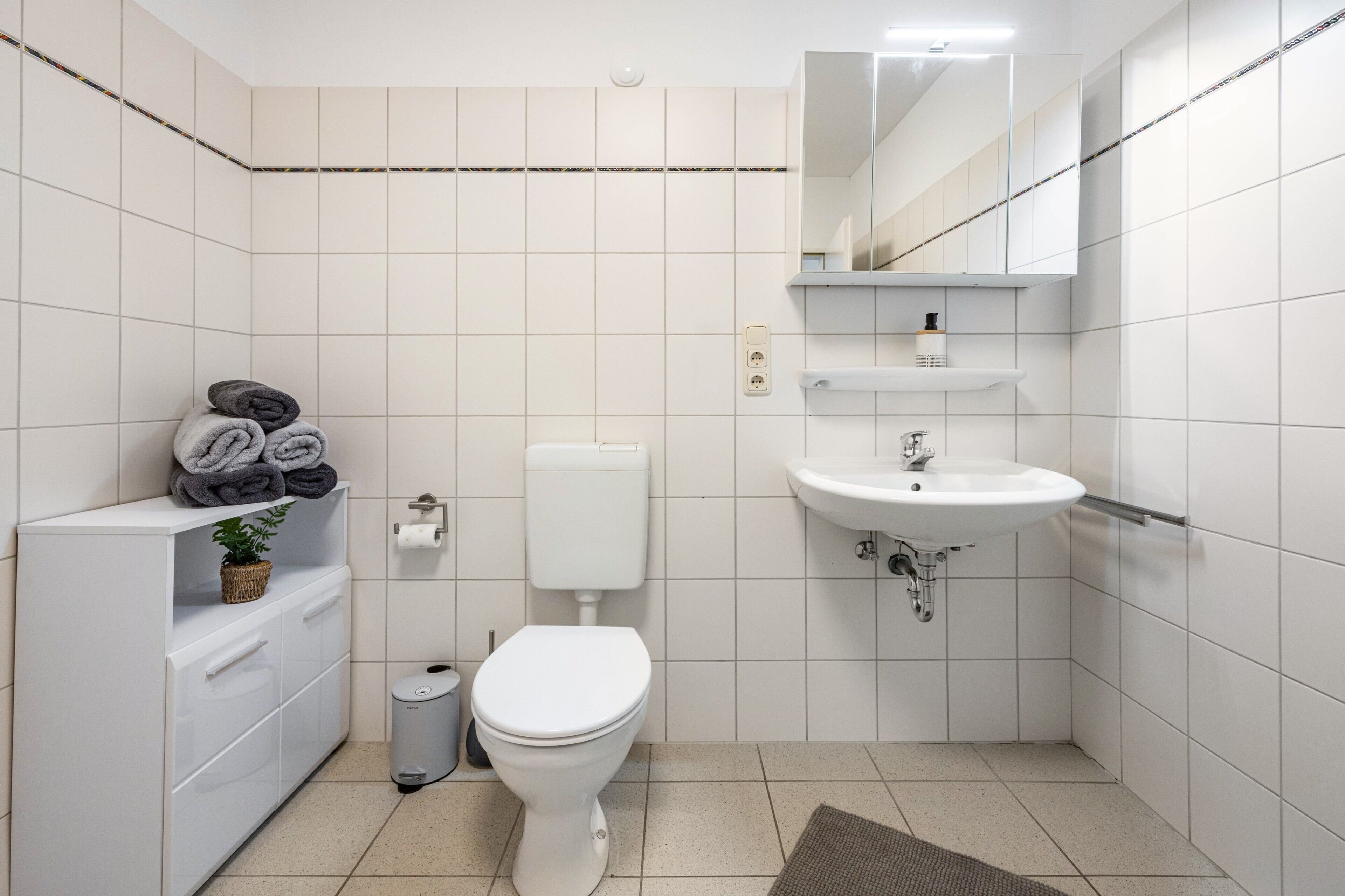 Une salle de bain moderne équipée de toilettes, d’un lavabo et d’un meuble de rangement.