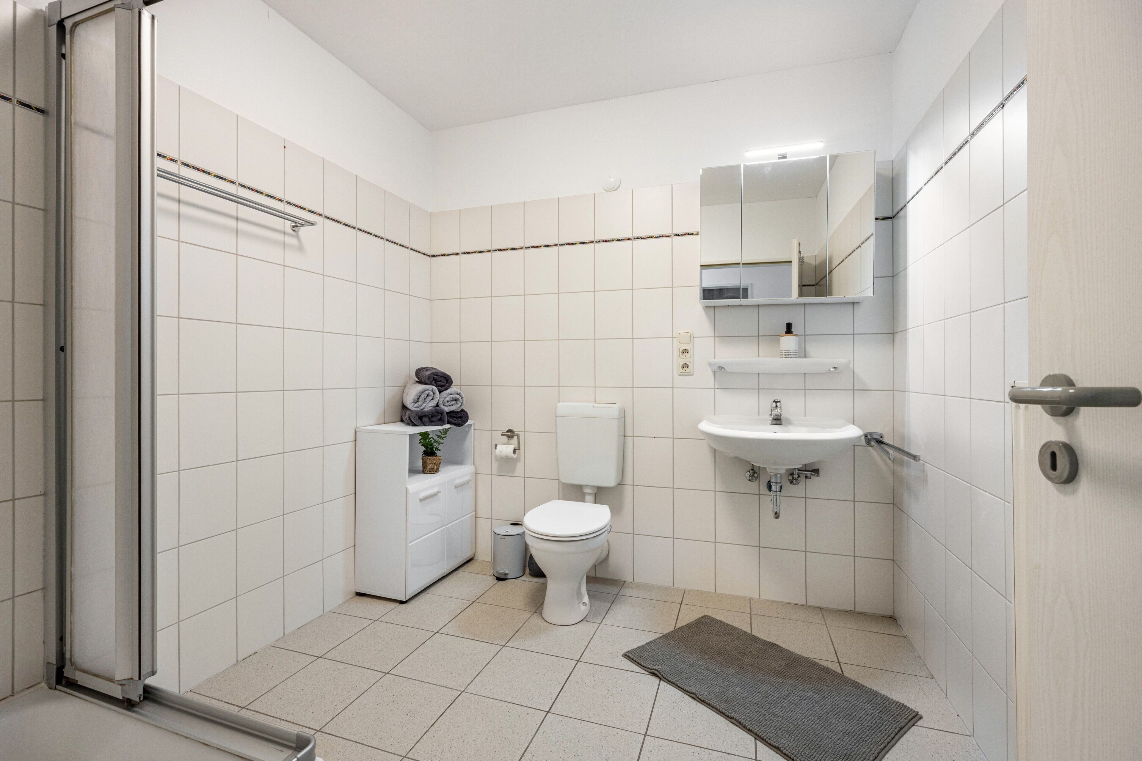 Een badkamer met toilet, wastafel, spiegel, handdoekrek en douche.