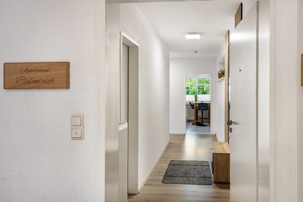 Un pasillo con un letrero de madera, una puerta, un radiador, una alfombra y vista a una habitación con una mesa y sillas.