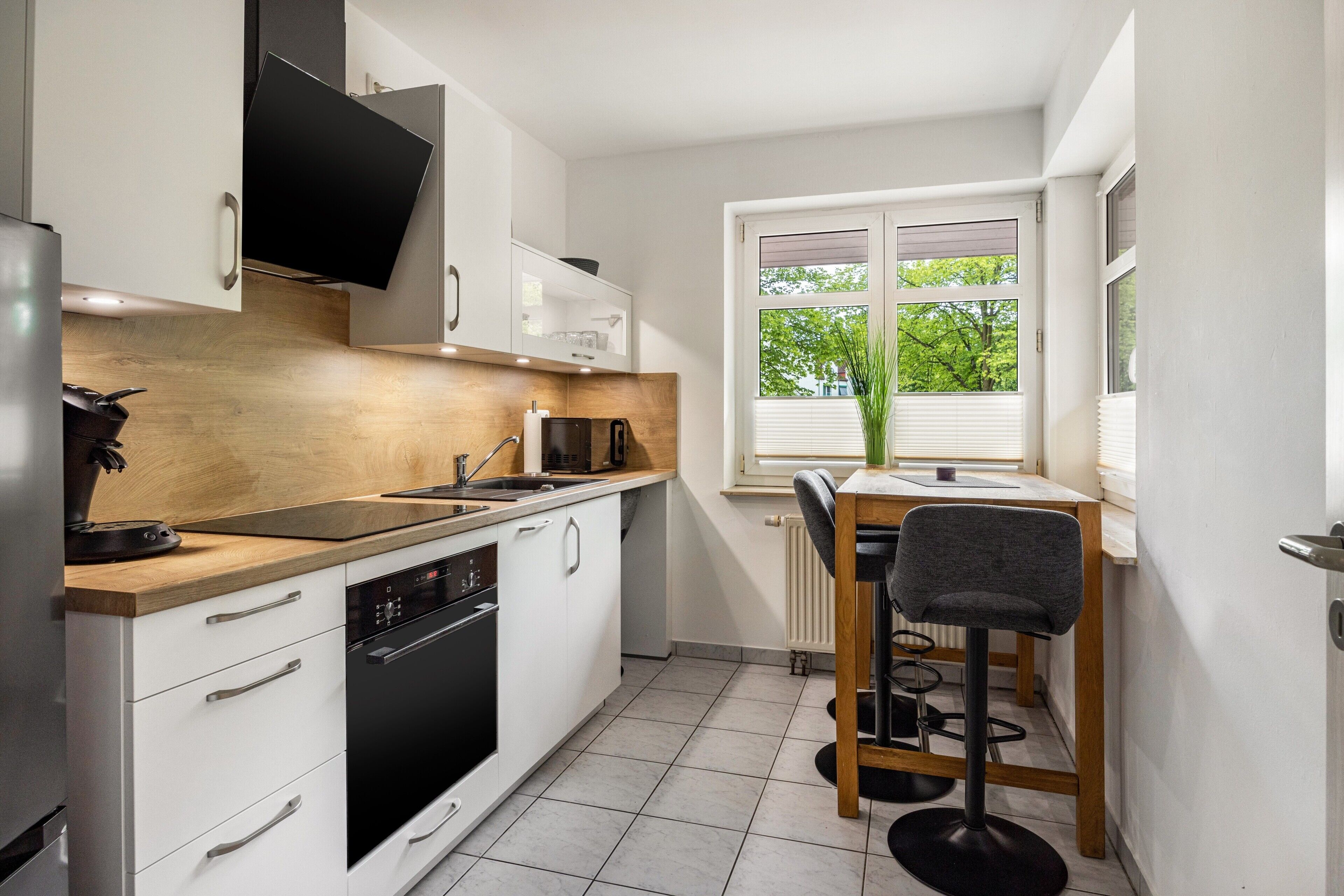 Een moderne keuken met witte kasten, een houten aanrecht, een ingebouwde oven en een eethoek met een tafel en stoelen.