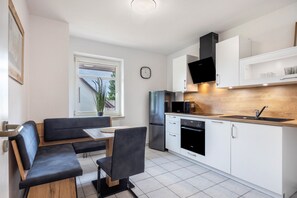 Una cocina moderna con armarios blancos, horno empotrado y refrigerador de acero inoxidable.
