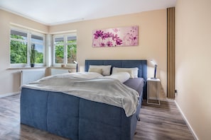 Un dormitorio con cama, ventana con vistas, radiador y lámpara fijada a la pared.