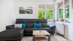 Uma sala de estar moderna com sofá seccional, uma pequena mesa de madeira e vista para o verde pela janela.