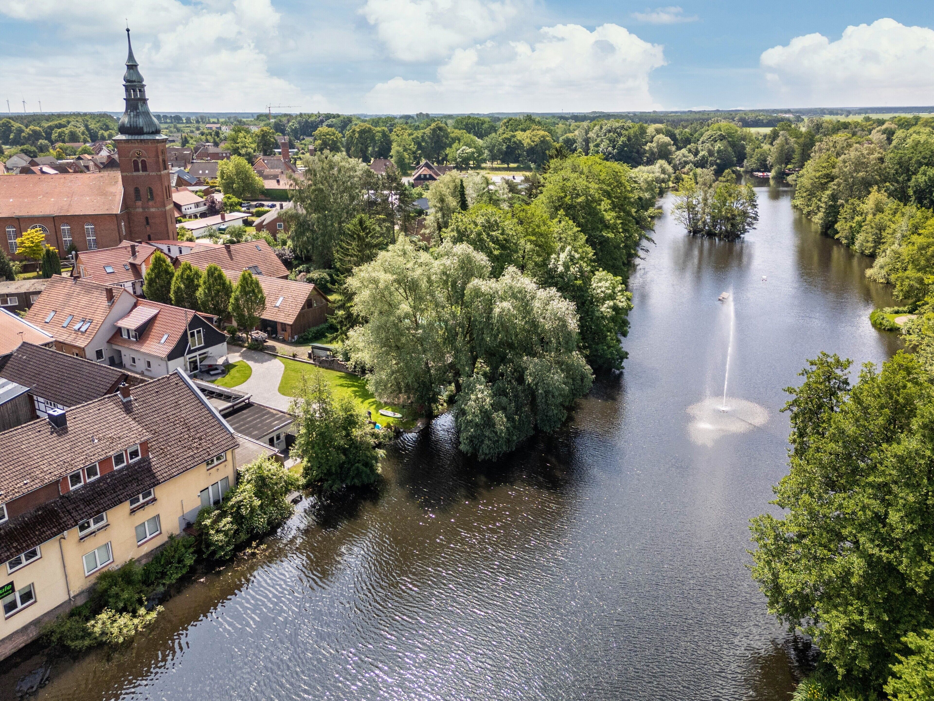 Een rivier die door een stad stroomt, met gebouwen aan één kant en een grote boom aan de andere kant.