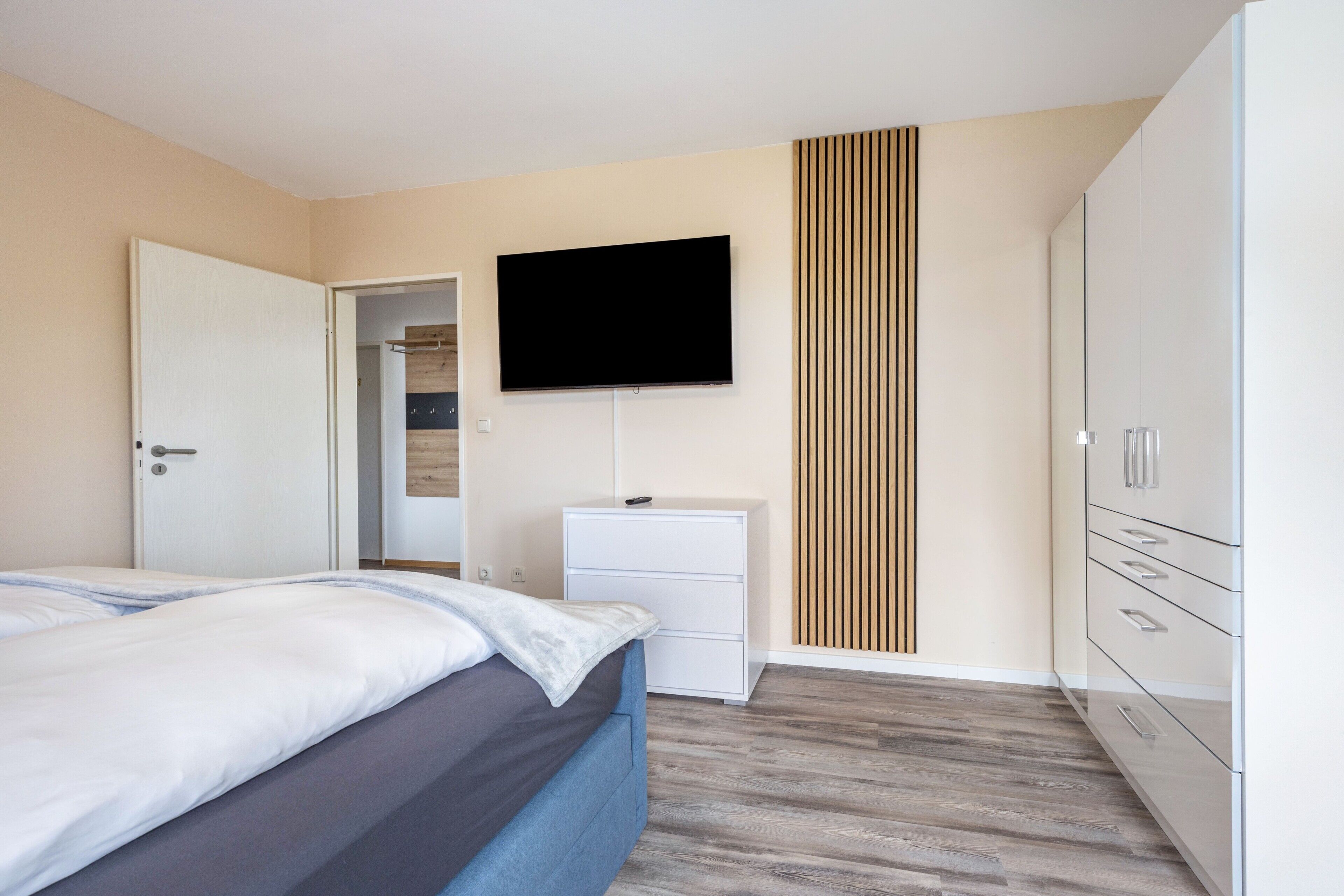 Ein Schlafzimmer mit Bett, Wandfernseher, Kleiderschrank und Nachttisch.