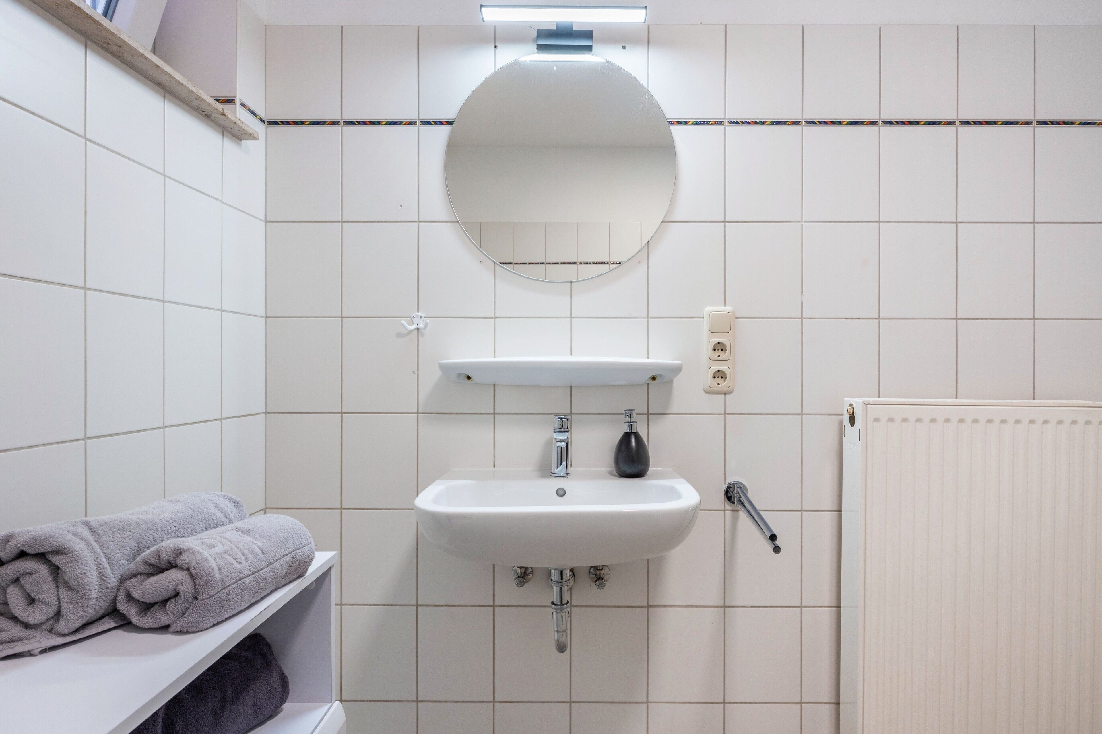 Ein Badezimmer mit Waschbecken, Spiegel, Handtuchhalter und Heizkörper.