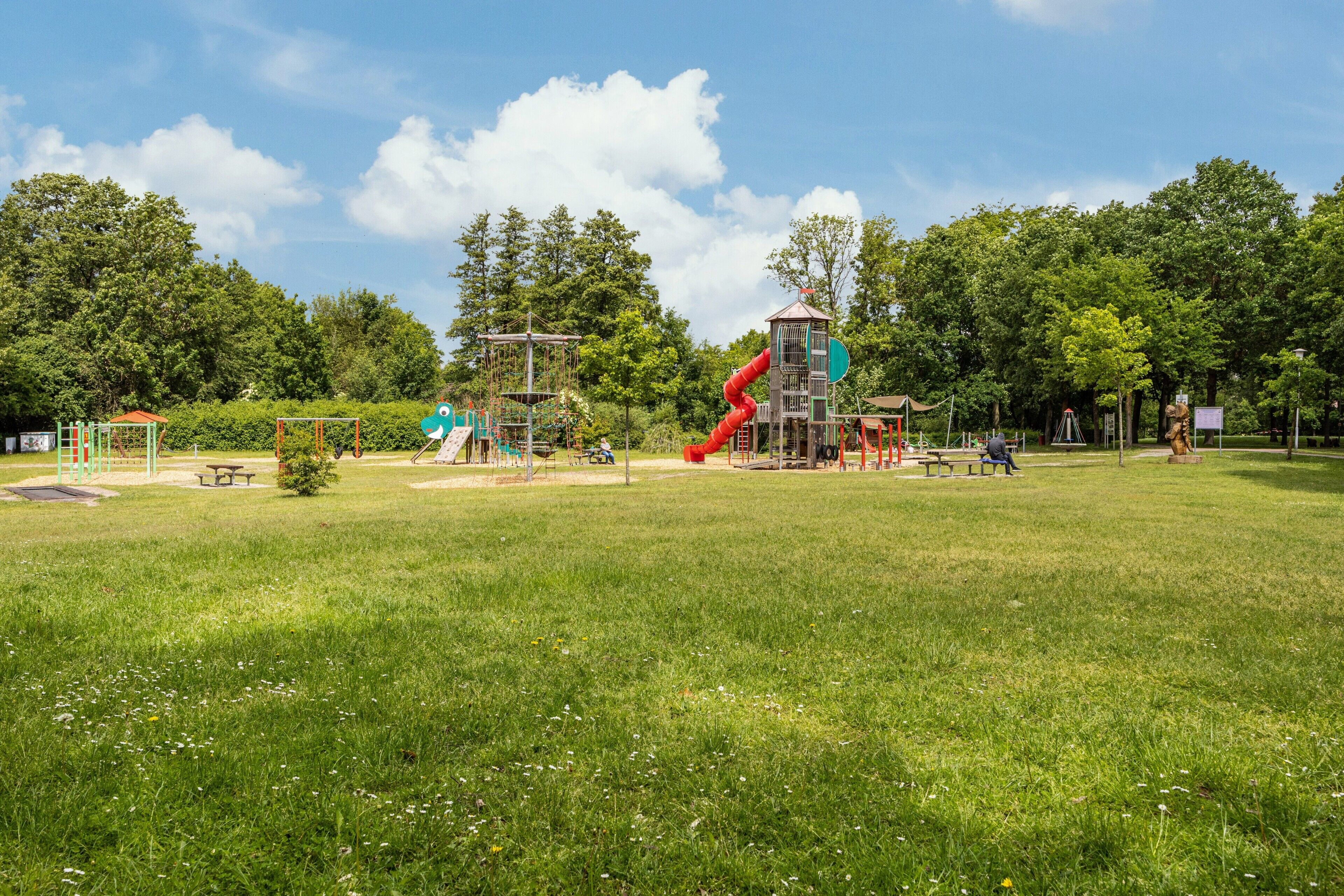 Ein Spielplatz mit Rutschen und Klettergerüsten, umgeben von Gras und Bäumen.