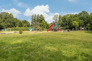 Un parque infantil con toboganes y estructuras para escalar, rodeado de césped y árboles.