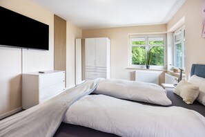 A bedroom with a bed, a TV, a wardrobe, a window with a view, and a radiator.