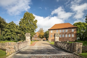A stone bridge leading to a brick building with a tiled roof, surrounded by trees and a clear sky. - Apartment 'Seaside' with Wi-Fi (Bad Bodenteich)