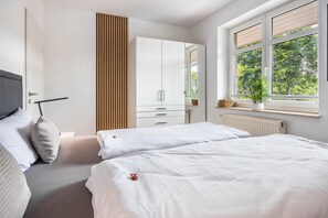 Un dormitorio con dos camas, un armario, un radiador y una ventana con vistas a árboles.