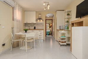 Una cocina moderna con armarios blancos, un comedor con mesa y sillas redondas, una estufa integrada y un televisor montado en la pared.