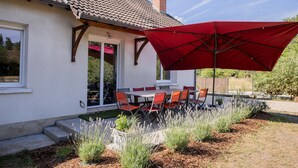 A house with a tiled roof, a red umbrella, and a patio with a table and chairs. - La Parenthèse de Sologne – Pool – Hot Tub – 25 min to Beauval (Gy-en-Sologne)