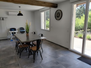 A dining area with a large table, chairs, a potted plant, and a clock on the wall.