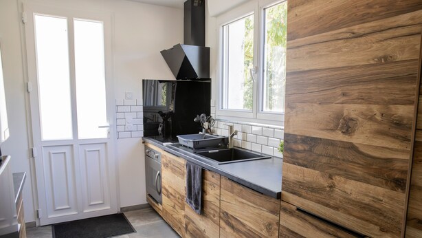 A modern kitchen with a wooden backsplash, a black range hood, and a window providing natural light. - La Parenthèse de Sologne – Pool – Hot Tub – 25 min to Beauval (Gy-en-Sologne)