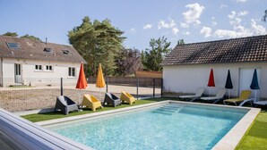 A rectangular swimming pool with a tiled deck, surrounded by a fence, and equipped with multiple lounge chairs and umbrellas. - La Parenthèse de Sologne – Pool – Hot Tub – 25 min to Beauval (Gy-en-Sologne)