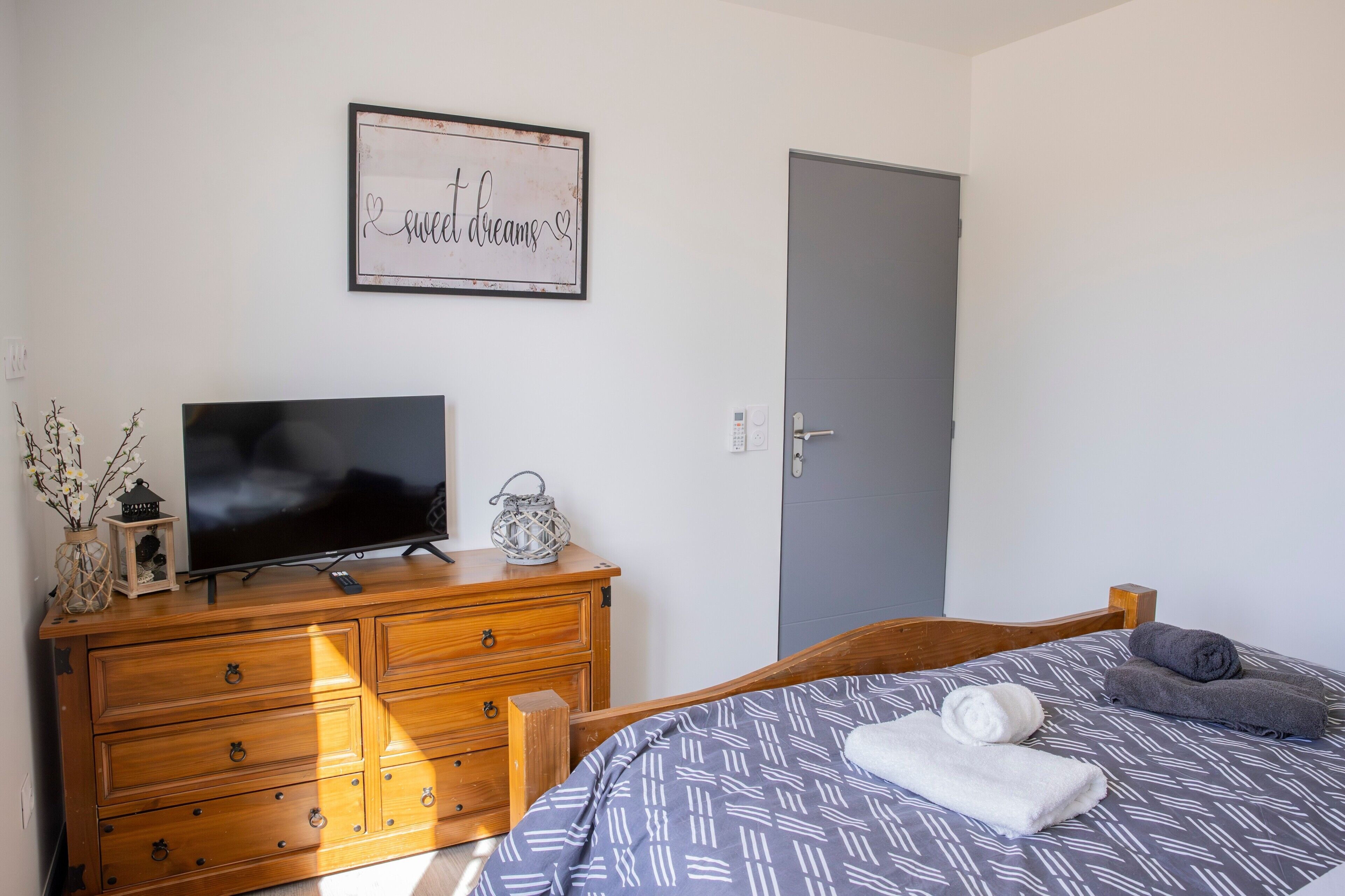Un dormitorio con cama, cómoda, televisor, puerta y una decoración en la pared.