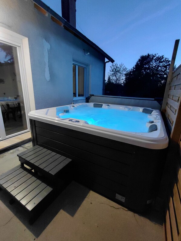 A hot tub with a wooden deck and a glass door leading to an outdoor area.