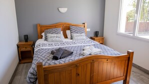 A neatly made bed with patterned bedding, a bedside table with a lamp, and a window with a view. - La Parenthèse de Sologne – Pool – Hot Tub – 25 min to Beauval (Gy-en-Sologne)
