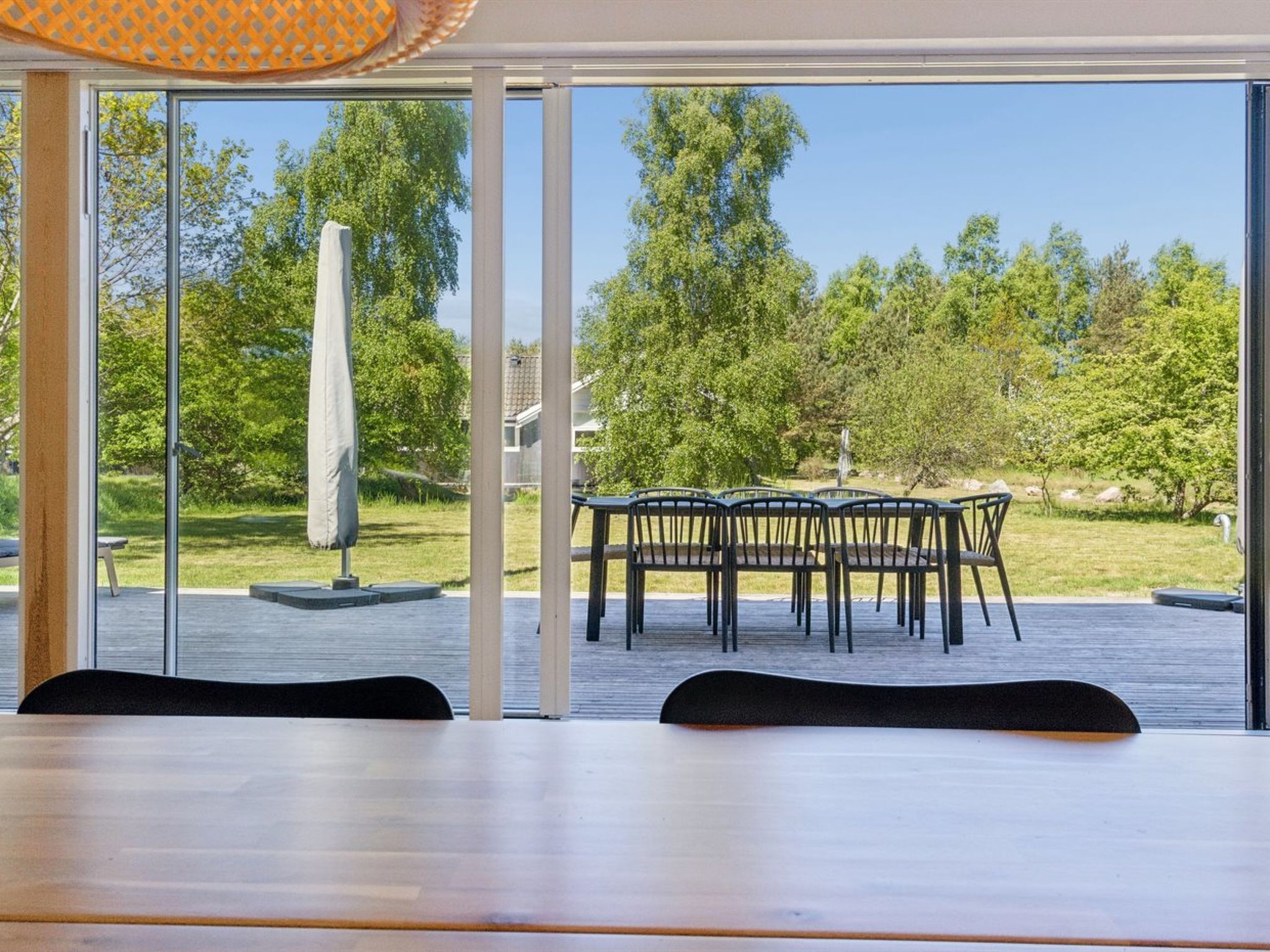 Ein moderner Außenbereich zum Essen mit Tisch und Stühlen, großen Fenstern und Blick auf eine grüne Landschaft.