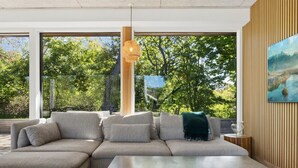 Een moderne woonkamer met een hoekbank, een salontafel en grote ramen met uitzicht op bomen en bergen.