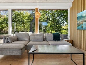 Ein modernes Wohnzimmer mit einer Eckcouch, einem Couchtisch und großen Fenstern mit Blick auf Bäume und Berge.