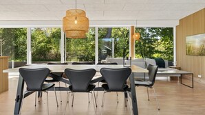 Een moderne eetruimte met een grote tafel, zwarte stoelen en een hangende rieten lamp.